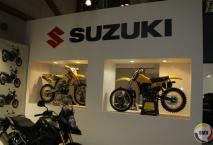 Een glimmende oldtimer Suzuki 250 cc, naast de fabrieks Suzuki van ClÃ©ment Desalle in de vitrine. 